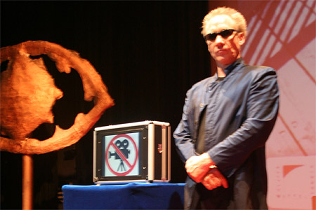Dobs Brugal neben seinem Cyber-Koffer, der auf seinem Bildschirm ein Kamera-Verbots-Logo zeigt ©Parabol